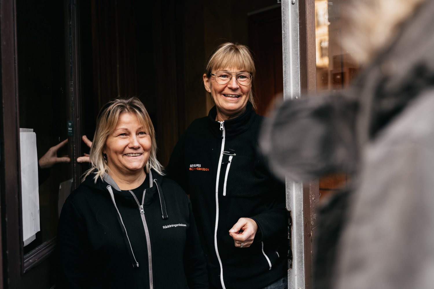 Två medarbetare på Räddningsmissionens frukostcafé välkomnar en gäst i dörren.