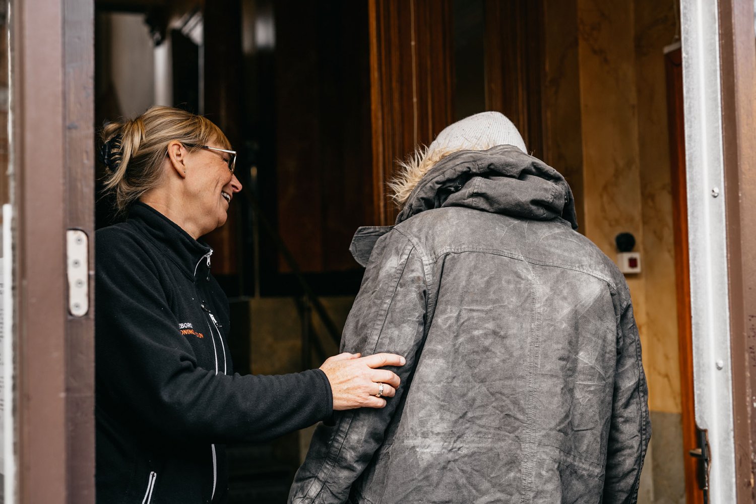 En man välkomnas in till Räddningsmissionens frukostcafé av en glad medarbetare.