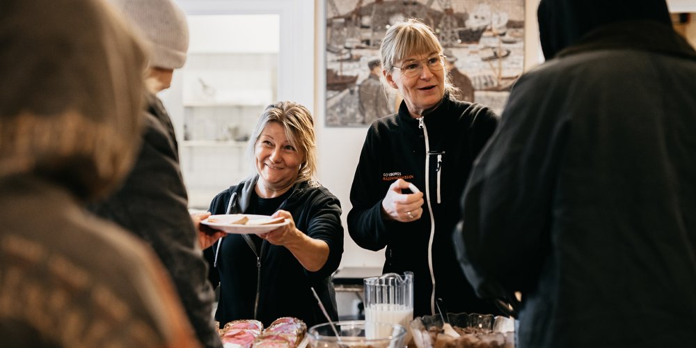 Två glada medarbetare serverar frukost till personer i hemlöshet på Räddningsmissionens frukostcafé.